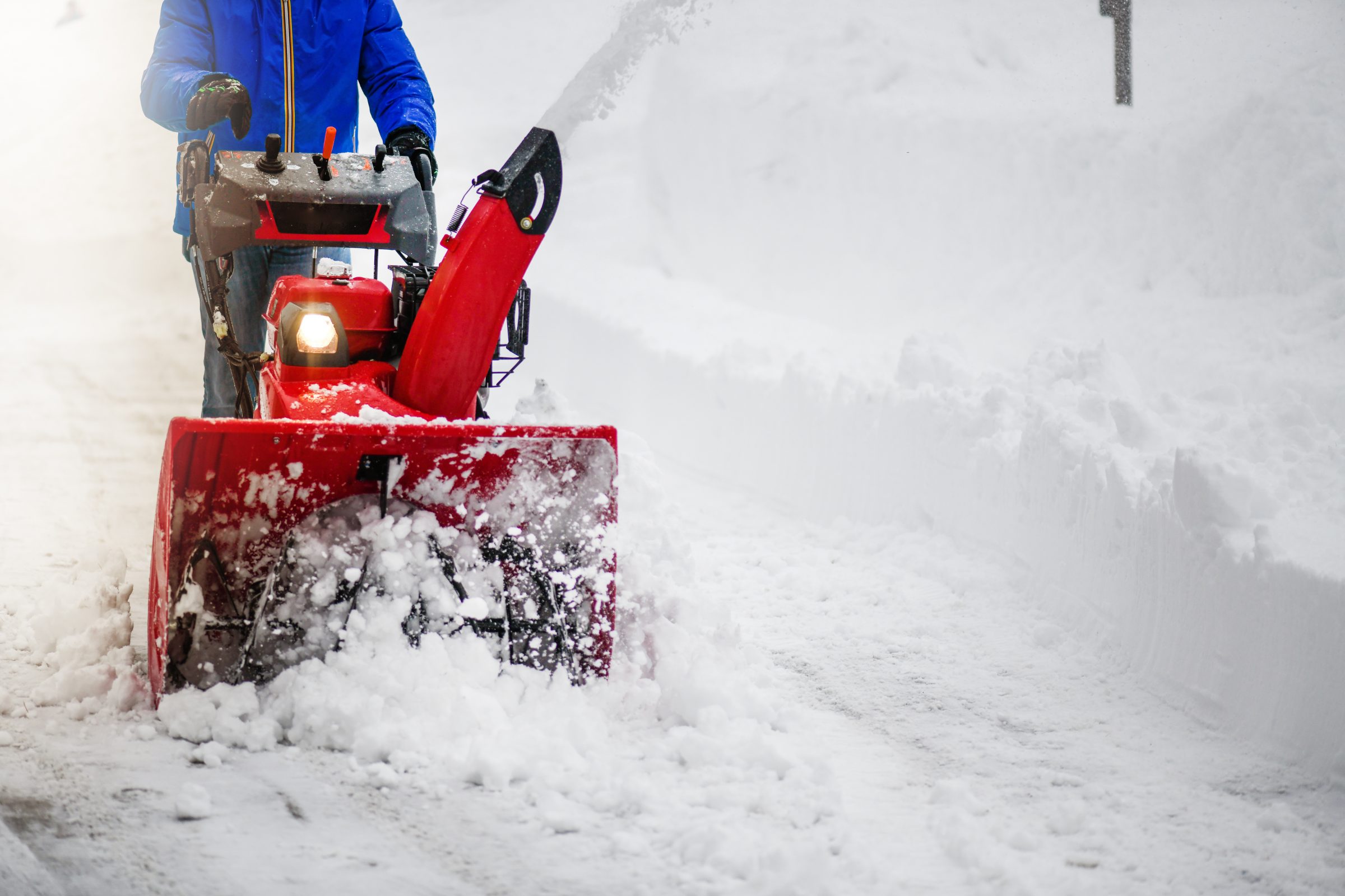 Person using snowblower to clear snowy pathway.