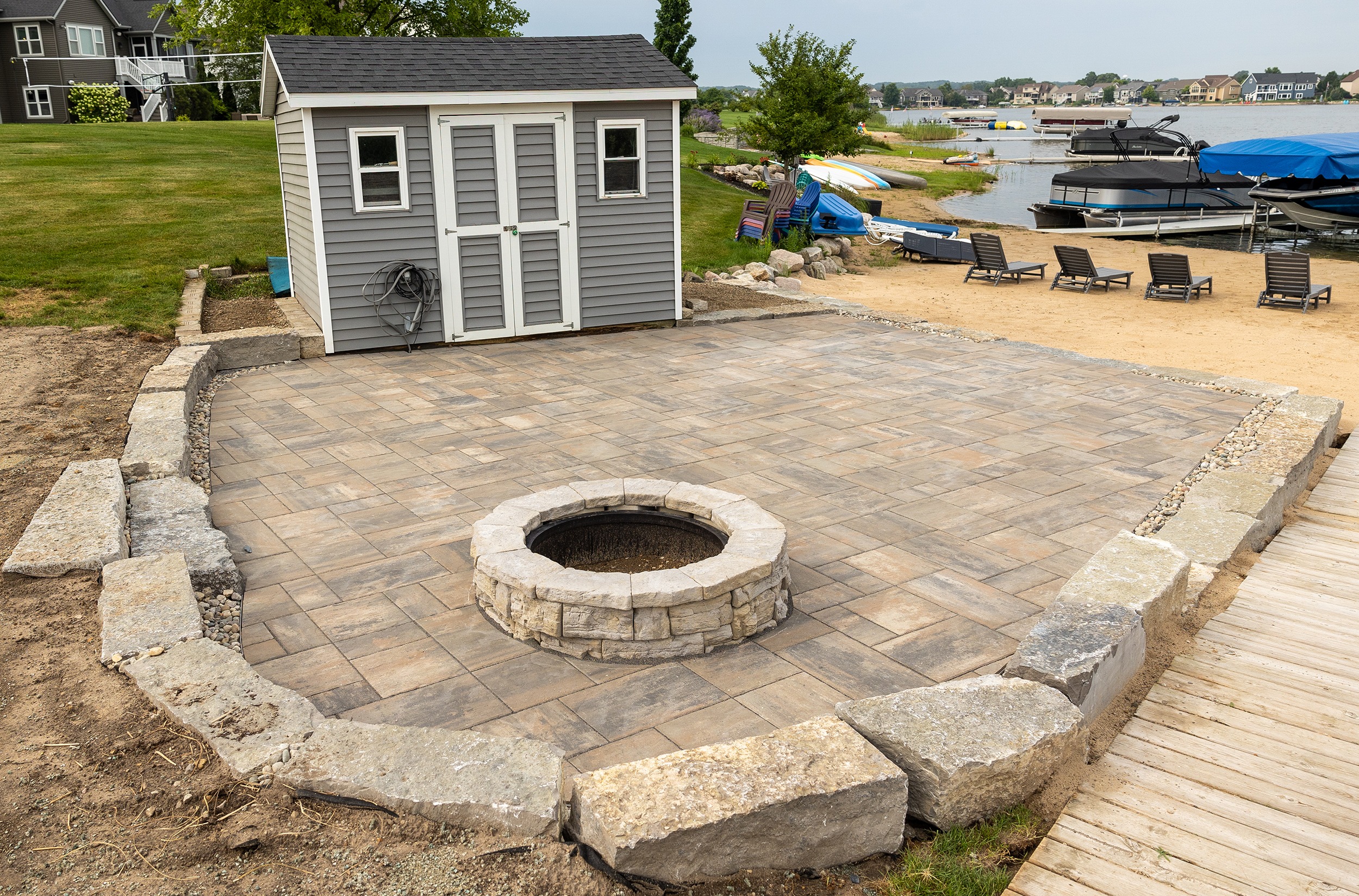 Lakeside patio with stone fire pit and shed.