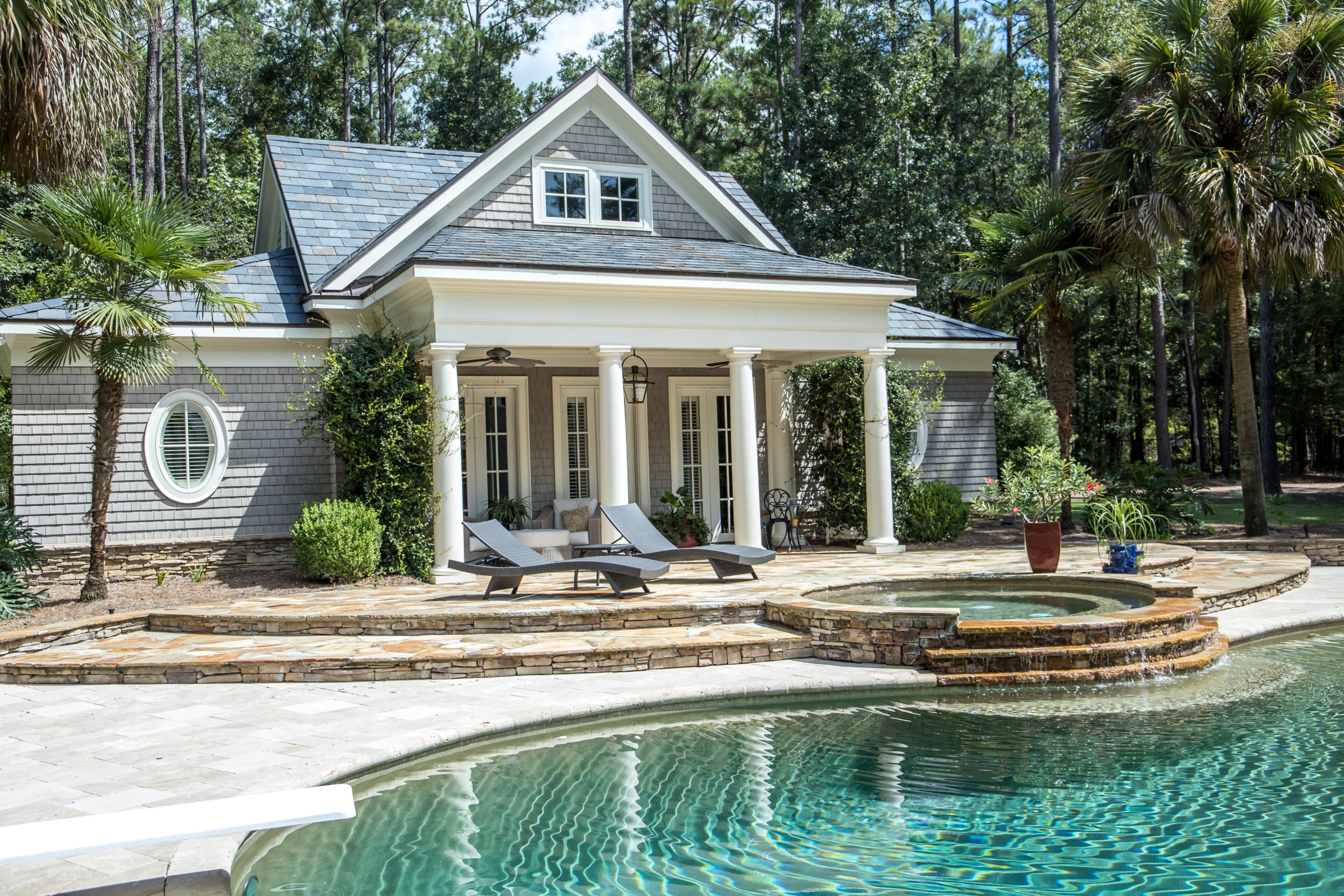 Elegant poolside house with chairs and greenery.