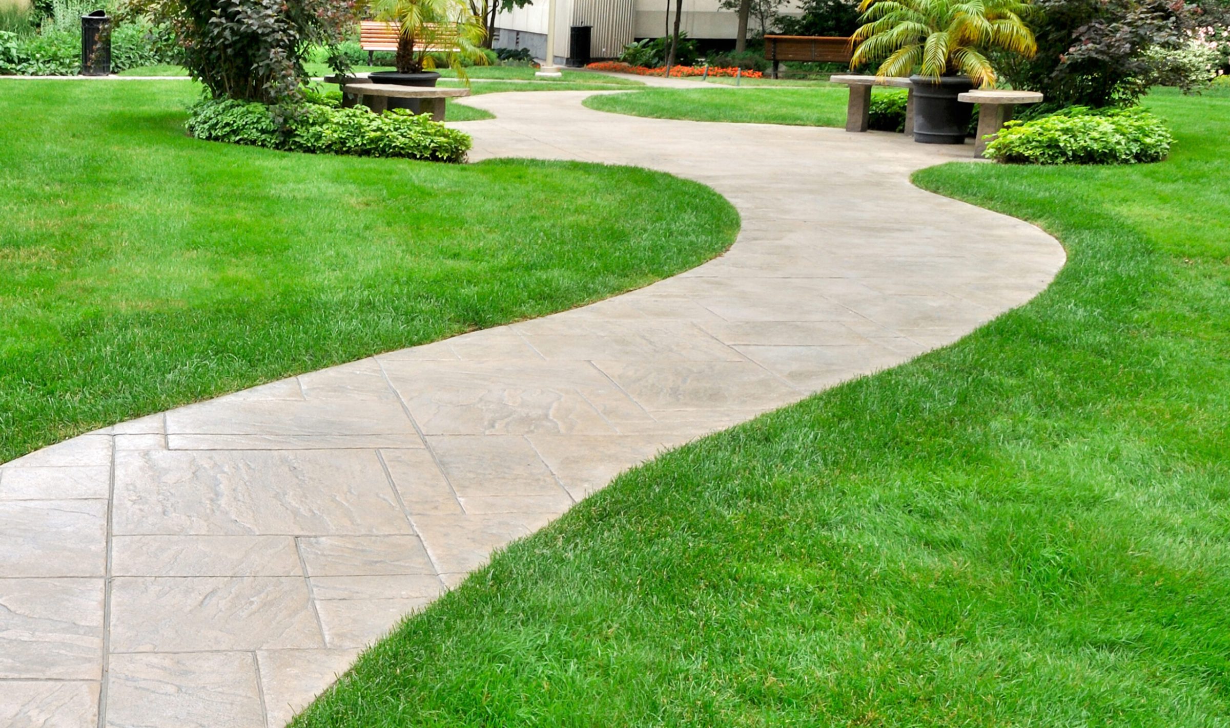 Curved garden pathway with benches and greenery.