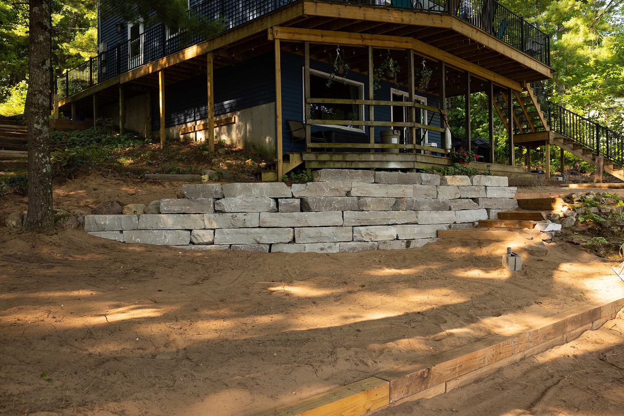 Wooden deck above stone retaining wall and sandy ground.
