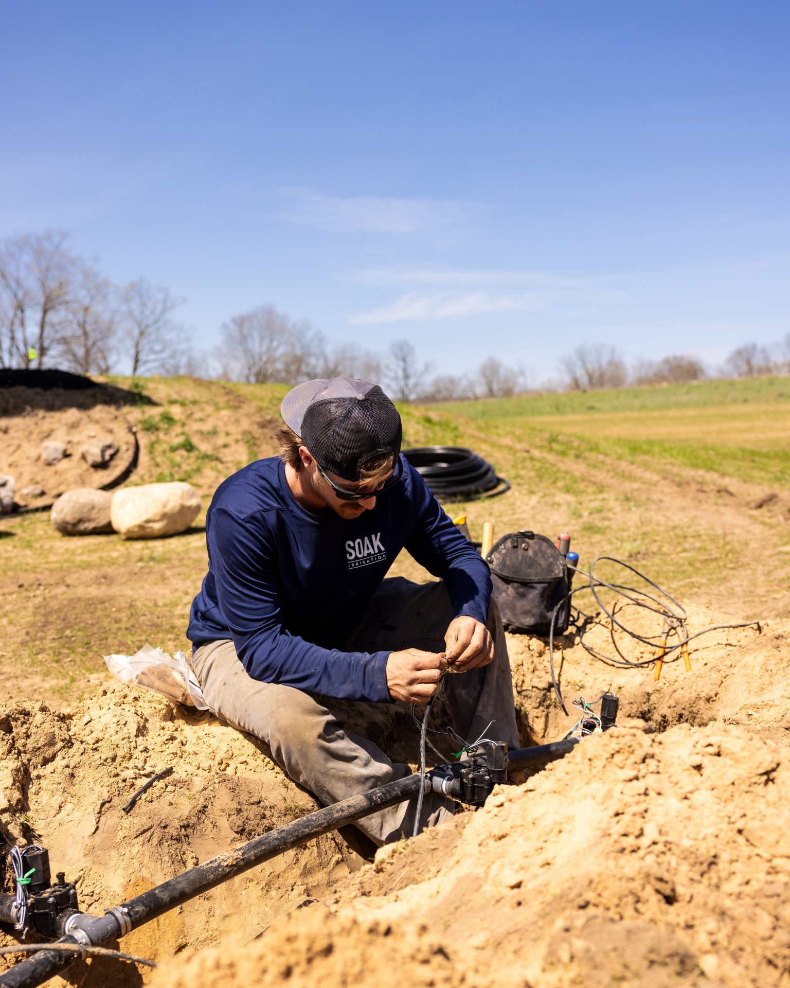 Worker installing irrigation system in sunny field.