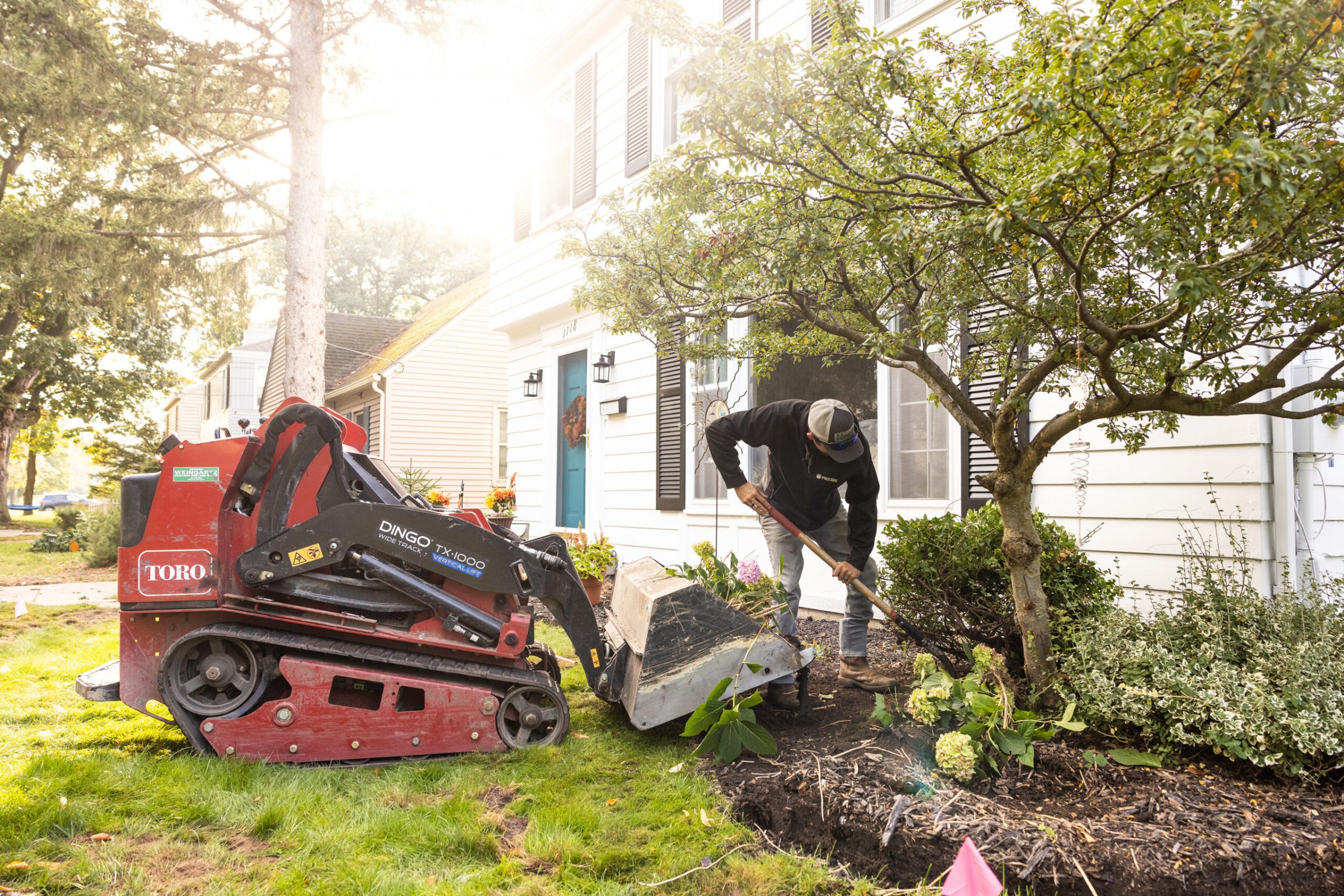 Worker landscaping with mini loader outside house