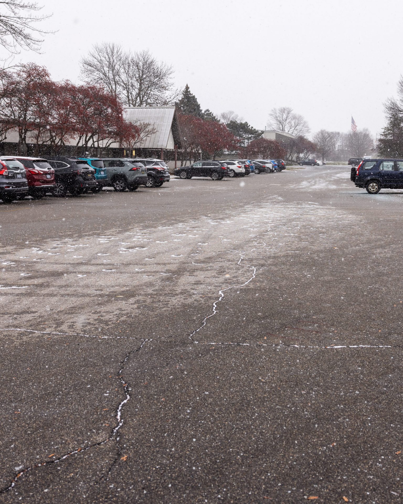 Snowy parking lot with cars and trees.