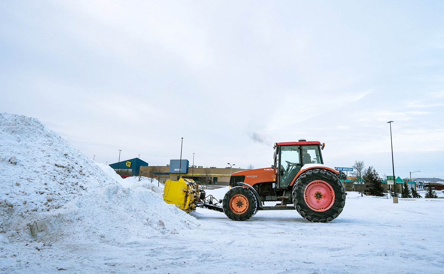 Tractor clearing snow in winter parking lot.