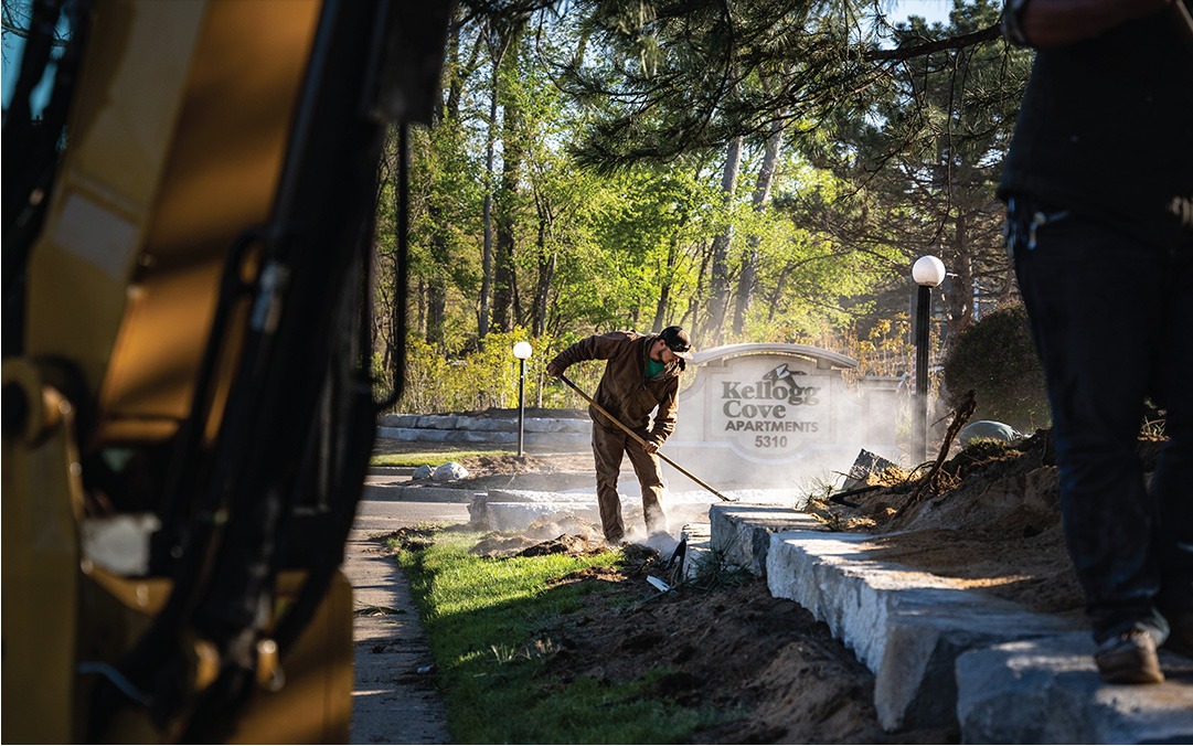 Worker landscaping near Kellog Cove Apartments sign