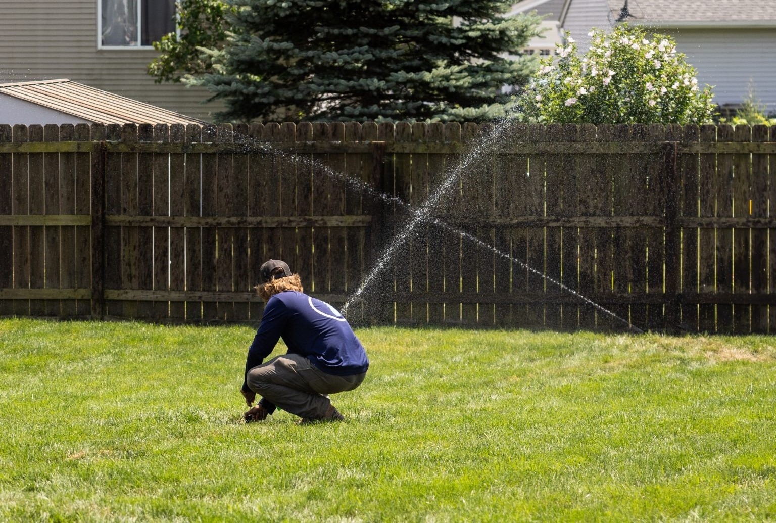 Person adjusting garden sprinkler in backyard lawn.