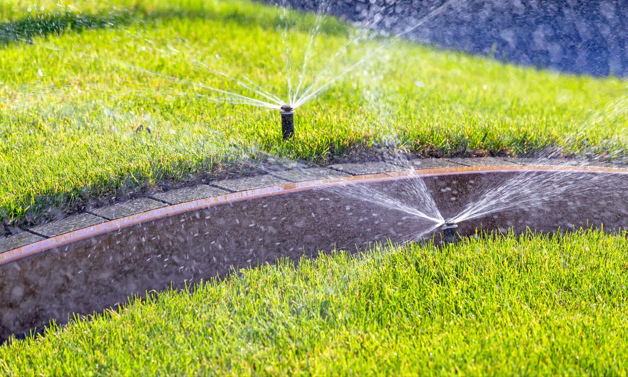 Automatic sprinkler heads watering green lawn along concrete curb