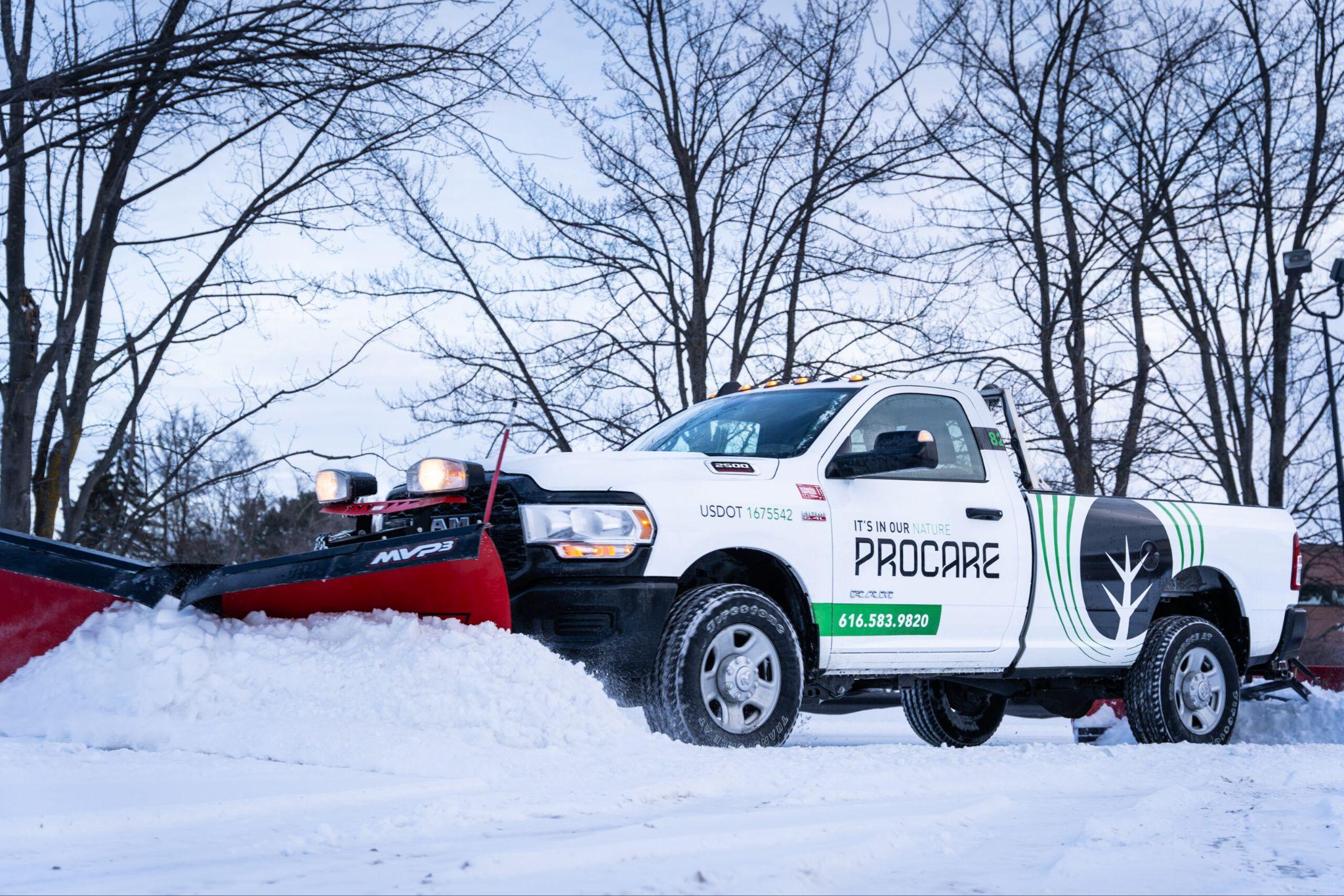 Commercial snow plow truck clearing snow in parking lot with company branding visible