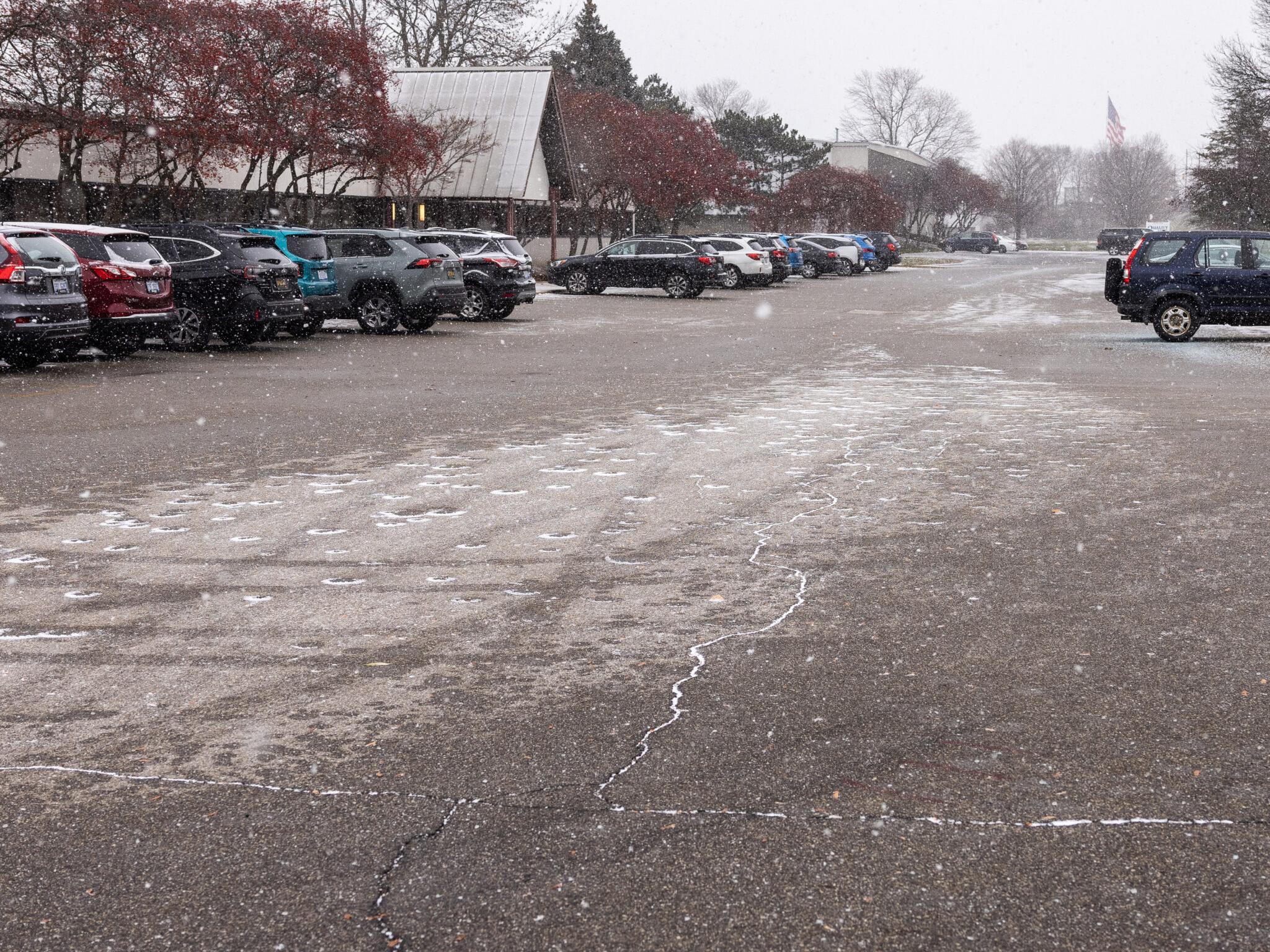 Icy parking lot with parked cars and light snowfall creating slick conditions