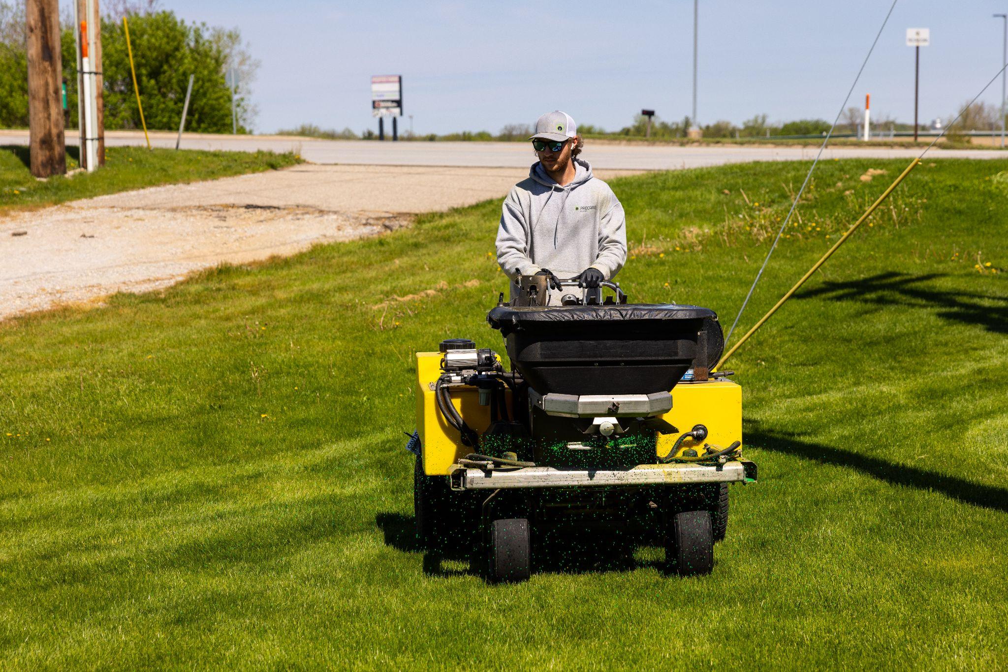 Lawn care worker applying fertilizer on grass using spreader machine