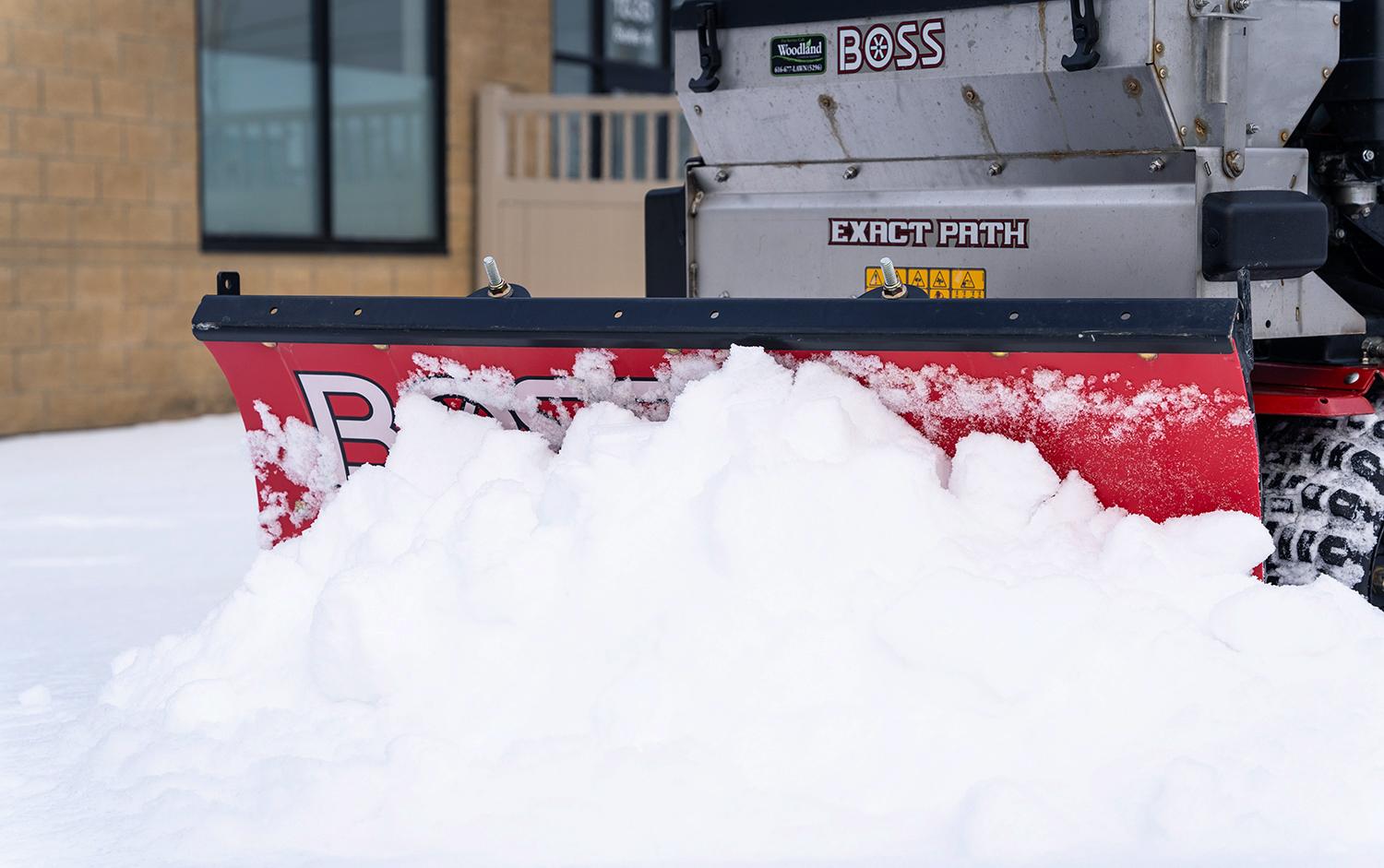 Snow plow blade pushing heavy snow near building during winter maintenance