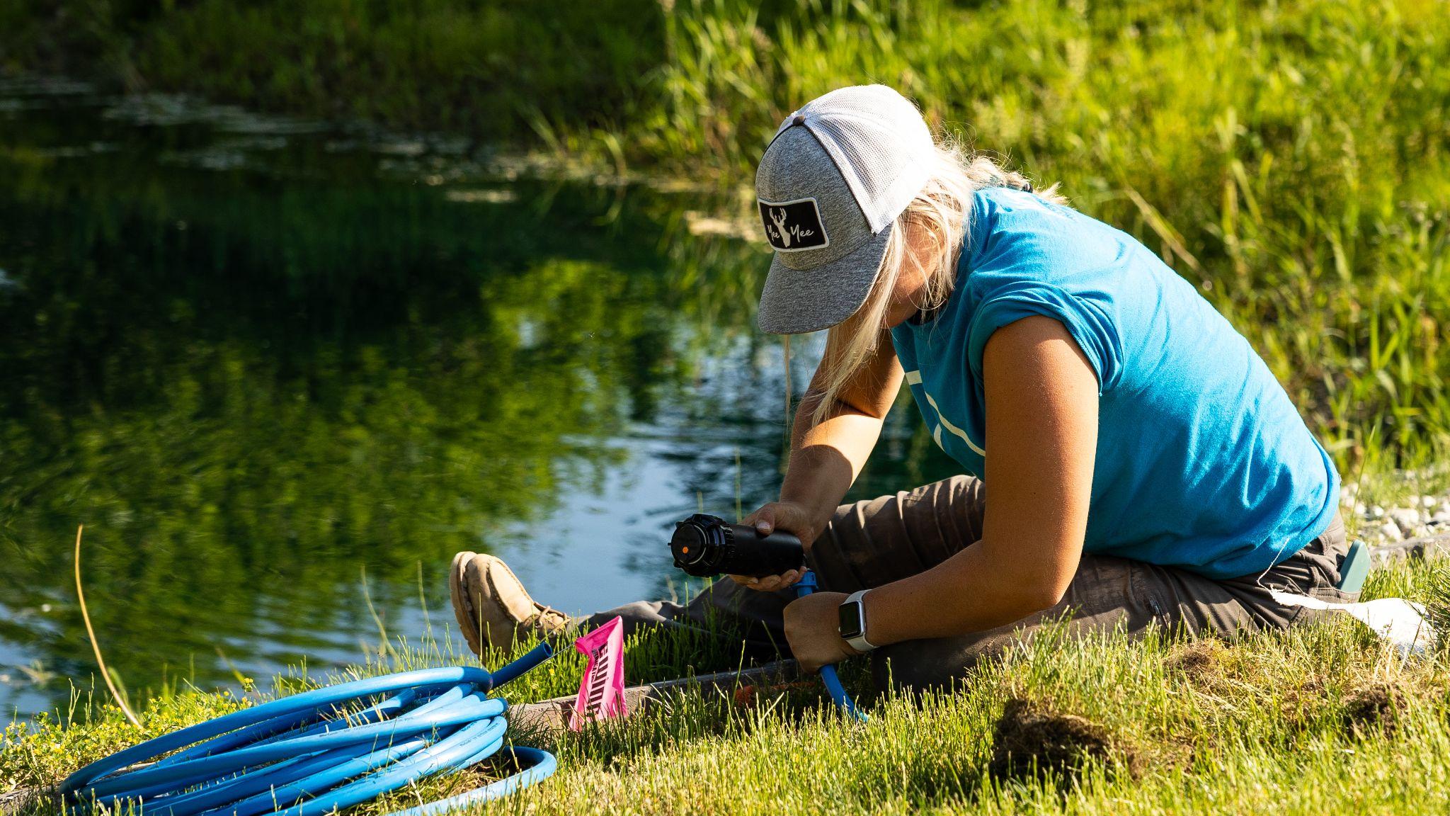 Technician repairing irrigation valve beside pond with tools and tubing
