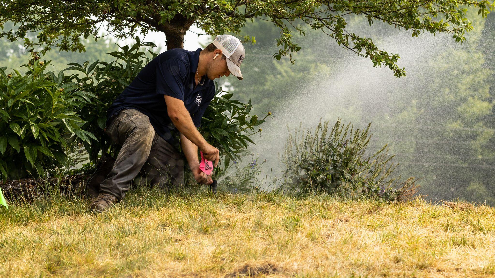 Technician repairing irrigation valve beside pond with tools and tubing