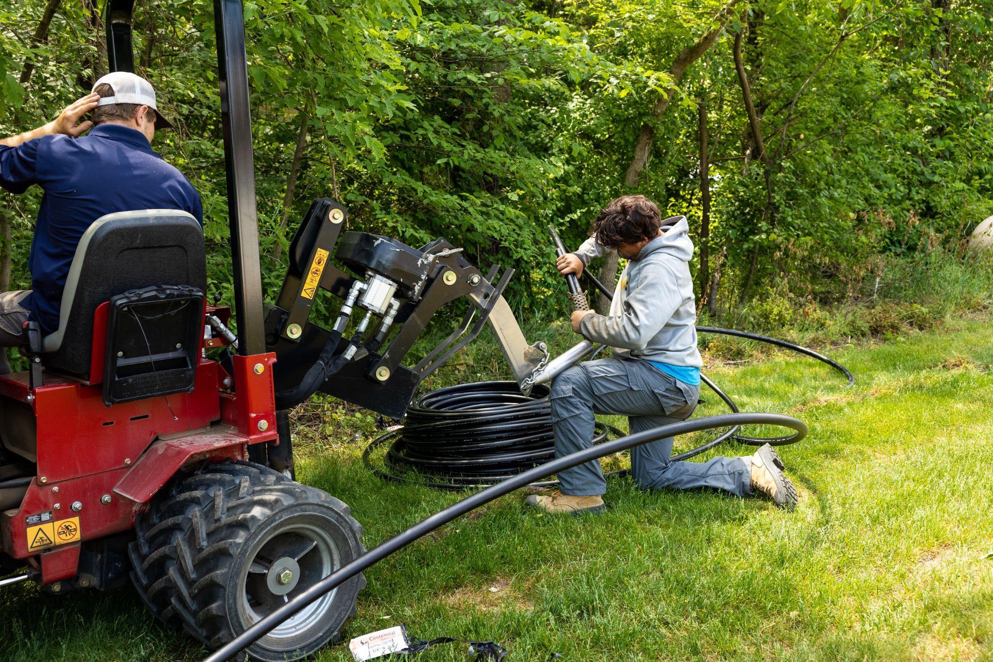Two workers installing underground irrigation piping using trenching machine